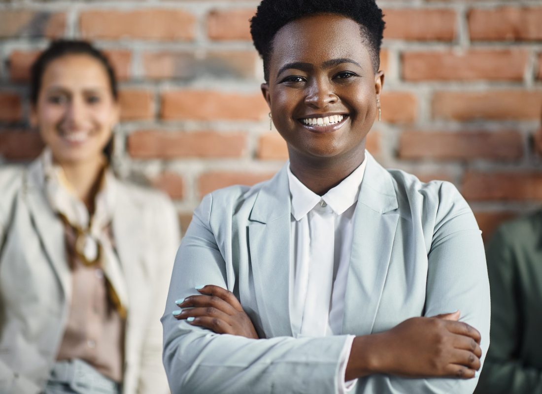 Confident African American female CEO standing with crossed arms in front of her business team and looking at camera.